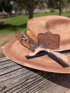 Coors Cowboy meets rancher hat!  Leather Coors Cowboy Patch on a wide brim rancher hat. Hand burned edges to look aged.  Layered soft fabric with silver chain band and naturally sourced feathers. ADD ON OPTIONS:  Want your initials added to the chain band for a custom hat!   This is a Vegan Suede Rancher Hat in tan color -hand burned to look aged This hat is one size fits most, Medium,  with an elastic inner band to fit size 55-59cm or  7 - 7¼  This hat is ready to ship. NOTICE OF NON-AFFILIATION AND DISCLAIMER: We are not affiliated, associated, authorized, endorsed by, or in any way officially connected with the brand shown or any of its subsidiaries or its affiliates. All related names, marks, emblems and images are registered trademarks of their respective owners. These are not officia Rustic Flat Brim Fedora For Kentucky Derby, Rustic Hat Bands For Kentucky Derby Festival, Rustic Fedora For Kentucky Derby And Country Events, Rustic Style Hat Bands For Kentucky Derby, Rustic Felt Hat For Kentucky Derby And Country Events, Rustic Brimmed Hat Band For Kentucky Derby, Rustic Wide Brim Hat Bands For Kentucky Derby, Country Style Fedora With Flat Crown For Country Events, Rustic Fedora With Flat Crown For Country Events