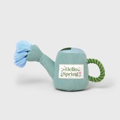 a green teapot with a blue handle on it and the words hello spring written in white