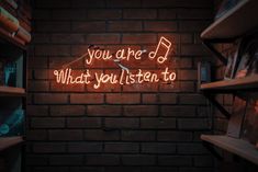 a neon sign that reads, you are d what you listen to on a brick wall