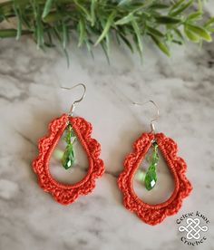 red crochet earrings with green beaded tears on marble surface next to plant