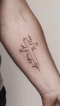 a cross tattoo on the arm with an arrow and leaves around it, in black ink