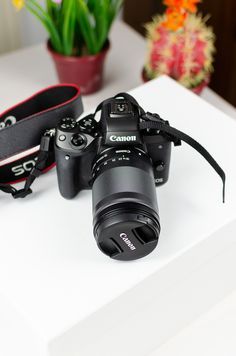 a camera sitting on top of a white table next to a flower pot and strap