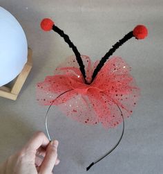 a hand is holding a headband made out of mesh and red pom - poms