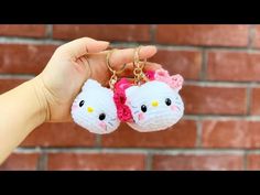 two hello kitty keychains are being held up by someone's hand in front of a brick wall