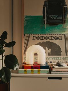 a table topped with books next to a potted plant and a painting on the wall