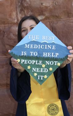 a woman holding up a graduation cap that says the best medicine is to help people not need it