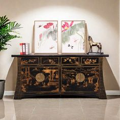 a black and gold dresser with two pictures on top of it next to a potted plant