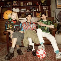 three young people sitting on a couch with a soccer ball in front of them and bookshelves behind them