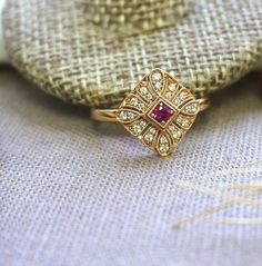 "One round center ruby set within a square filigree,all around with larger in size diamonds on outer ring face and other slightly smaller diamonds on inner ring face.Hollow back design allows the light to penetrate through the ring and brings out the shines of the stone. Curved and low profile so it sits close to your finger. Our small art deco series make perfect choice for daily wear. Dainty and delicate design yet still tasteful and classy. Material: 1 ruby approx.0.09 carat. 24 diamonds of 0 Art Deco Ruby Ring With Center Stone, Art Deco Ruby Ring With Rose Cut Diamonds, Art Deco Ruby Ring With Diamond, Art Deco Gold Ruby Ring, Art Deco Red Diamond Ring, Art Deco Ruby Ring With Diamond Cut For Wedding, Art Deco Yellow Gold Ruby Ring For Wedding, Art Deco Ruby Wedding Ring, Art Deco Jewelry Rings