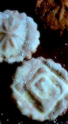 three cookies are covered in powdered sugar on top of a black plate with other pastries