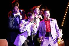 a group of young men standing next to each other in front of a stage curtain