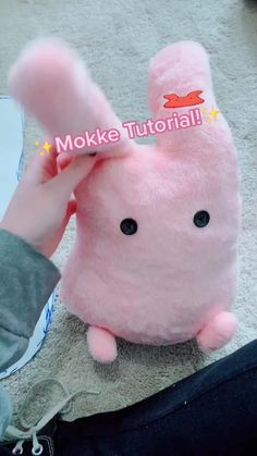 a pink stuffed animal sitting on top of a floor next to someone's hand