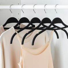 clothes hanging on hangers in front of a white wall and two beige tops with black straps