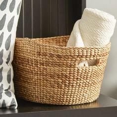 a woven basket sitting on top of a wooden table next to a pillow and blanket