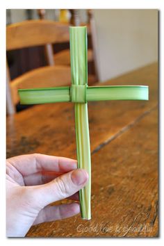 a hand holding a green cross on top of a wooden table