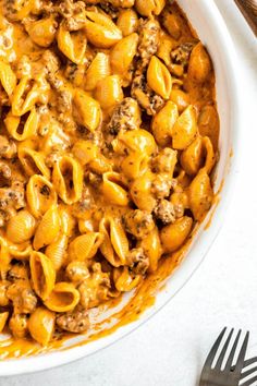 a white bowl filled with macaroni and cheese on top of a table next to silverware