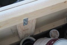 the bottom half of a wooden shelf with paint cans in it and two buckets below