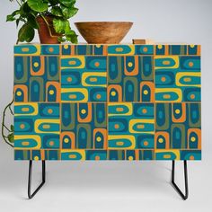 a potted plant sitting on top of a wooden stand next to a blue and yellow patterned cabinet