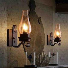 two lights are on the wall in front of a mirror and vases with candles