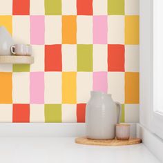 a white vase sitting on top of a counter in front of a colorful wallpaper