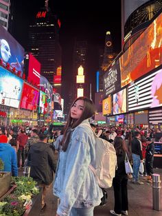 a woman standing in the middle of a busy street at night with lots of people