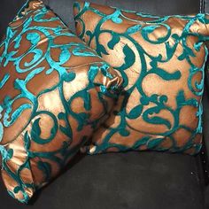 two brown and teal decorative pillows on a black couch with blue piping around the edges