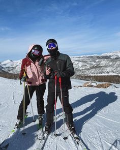 two skiers pose for a photo on the top of a mountain in ski gear