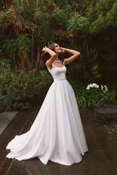 a woman in a white wedding dress posing for the camera with her hands behind her head