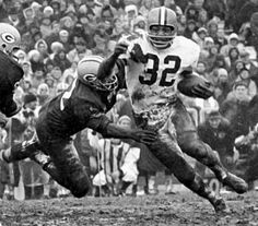 an old black and white photo of a football player running with the ball in his hands