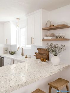 a kitchen with white cabinets and marble counter tops, wooden stools and open shelving