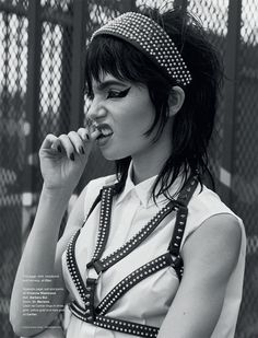 a woman with black and white makeup is holding her hand to her mouth while standing in front of a fence