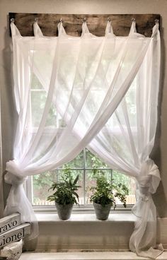 the window is decorated with white curtains and potted plants