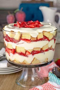 a cake with strawberries and cream is on a glass platter next to plates