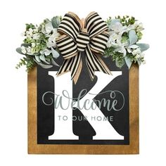 a wooden sign that says welcome to our home with a bow and flowers on it