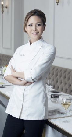 a woman in a chef's coat standing next to a table with silverware on it