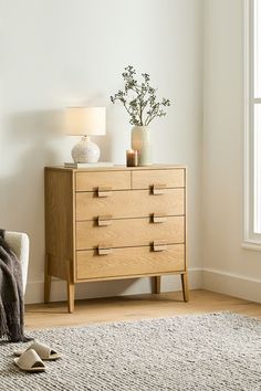 a living room with a white chair and wooden dresser next to a lamp on top of a rug