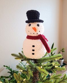 a knitted snowman ornament sitting on top of a christmas tree branch