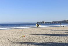 people are walking on the beach with their surfboards in front of an ocean pier