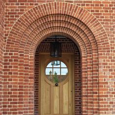 an arched wooden door with a lantern on the side and brick wall behind it, in front of a window