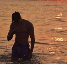 a man standing in the water at sunset with his hand up to his ear and head