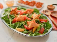 a salad with tomatoes, lettuce and other vegetables on a table next to utensils