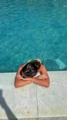 a woman sitting in front of a pool with her head on her hands and arms behind her back