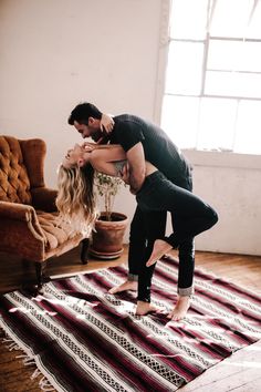 a man and woman dancing on a rug in front of a couch with potted plants