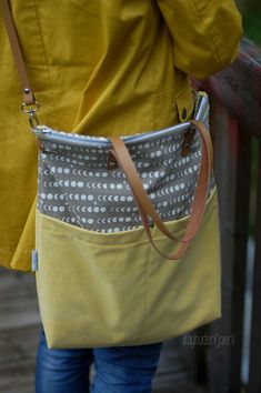 a woman carrying a yellow and gray purse on her back while standing next to a wooden bench