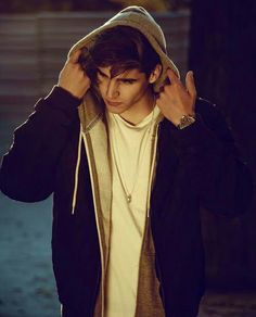 a young man wearing a hoodie and holding his hands up to his ears while walking down the street