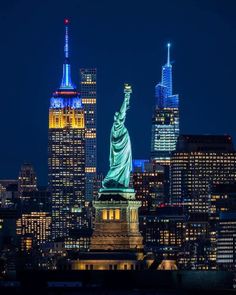 the statue of liberty is lit up at night in new york city, with skyscrapers behind it