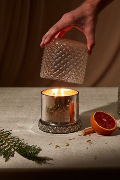 a person is pouring orange juice into a small glass candle holder with an orange slice on the side