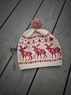 a red and white knitted hat sitting on top of a wooden floor next to a purple flower