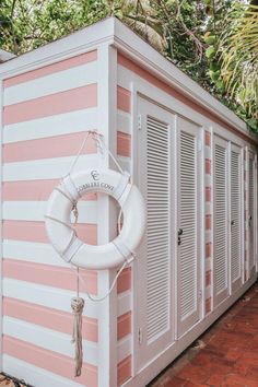 a white life preserver hanging on the side of a pink and white building with shutters