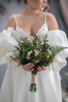 a woman in a white dress holding a bouquet of flowers and greenery on her wedding day